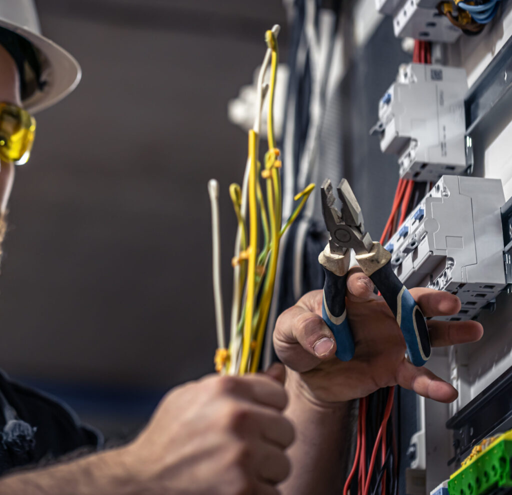 A male electrician works in a switchboard with an electrical connecting cable.